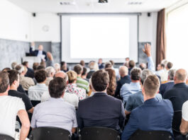 President of the management board presents past year company performance at annual general meeting of shareholders. Businesspeople with raised hands voting on resolutions of assembly. Copyright: kasto - stock.adobe.com