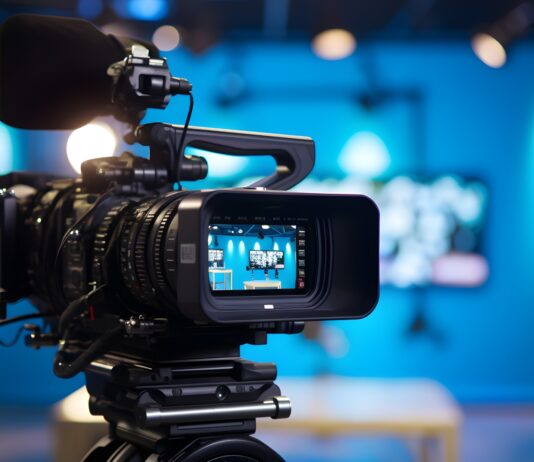 Modern video camera with a digital display recording an interview in a TV show studio. Blurry background. Mass media, television, and technology concepts. Behind the scenes of making of movie and TV