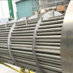 Großer industrieller Wärmetauscher mit mehreren parallel angeordneten Metallrohren. Die zylindrische Struktur hat eine runde Endplatte mit vielen Löchern, durch die die Rohre hindurchgehen.