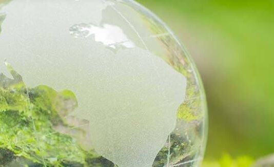 H2 Core: „In allen Weltregionen gibt es Initiativen für Wasserstoff-Projekte“ Das Bild zeigt einen transparenten Globus mit eingeätzten Kontinenten, insbesondere Nord- und Südamerika. Der Globus steht vor einem lebhaften grünen Hintergrund, der ein Natur- oder Umweltthema vermittelt.