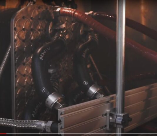 Mutares übernimmt Cikautxo Rubber & Plastic Components Nahaufnahme einer industriellen Anlage mit metallischen Rohren, Schläuchen und einem Plattenwärmetauscher. Die Rohre sind mit Kupplungen verbunden, und die Umgebung wirkt technisch.