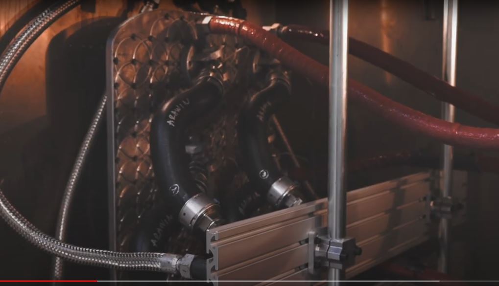 Nahaufnahme einer industriellen Anlage mit metallischen Rohren, Schläuchen und einem Plattenwärmetauscher. Die Rohre sind mit Kupplungen verbunden, und die Umgebung wirkt technisch.