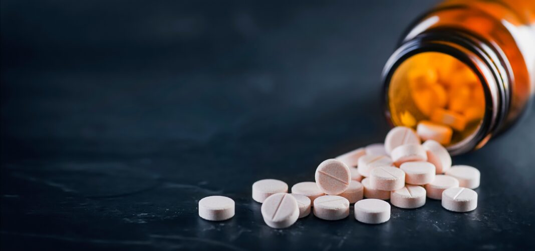 Weiße medizinische Pillen oder Tabletten mit einer Flasche auf schwarzem Hintergrund. Nahaufnahme mit Platz für Text.