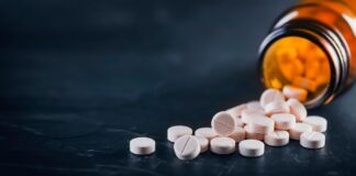 Weiße medizinische Pillen oder Tabletten mit einer Flasche auf schwarzem Hintergrund. Nahaufnahme mit Platz für Text.