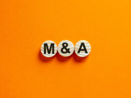 Das Bild zeigt die Buchstaben "M and A" auf Holzscheiben vor einem orangefarbenen Hintergrund. Geschäftskonzept mit Freiraum für Text.