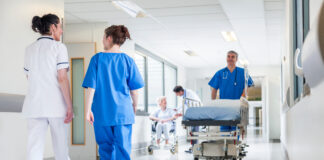 Symbolbild Krankenhaus (Male nurse pushing stretcher gurney bed in hospital corridor with doctors & senior female patient.) Copyright: spotmatikphoto - stock.adobe.com
