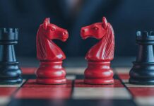 Investor placing chess pieces on a board shaped like a stock graph with bull and bear pieces, stocks, strategic market positioning. Copyright: KENZOGROW - stock.adobe.com