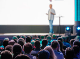 Symbolbild. Speaker delivering a presentation to a large audience at a business conference in a modern venue. Engaged attendees listen attentively. Copyright: Anton Gvozdikov - stock.adobe.com