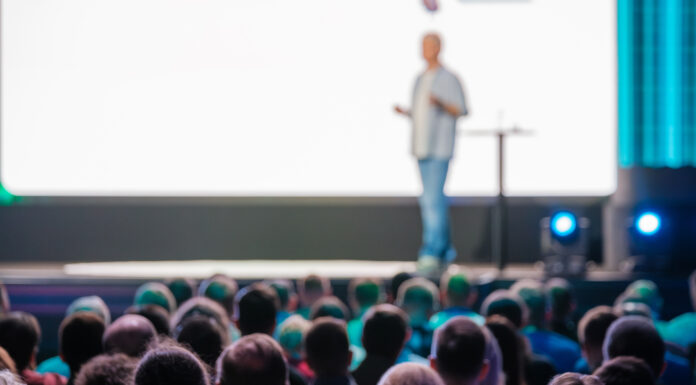 Die Zukunft der Hauptversammlung: Virtuell und Präsenz: Beim Hauptversammlungsformat gibt es kein „One Size fits all“ Symbolbild. Speaker delivering a presentation to a large audience at a business conference in a modern venue. Engaged attendees listen attentively. Copyright: Anton Gvozdikov - stock.adobe.com