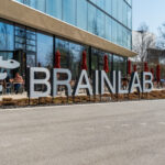 Brainlab lettering in front of the headquarters in Munich Riem with blue sky and sunshine. Copyright: Olaf Gedanitz - stock.adobe.com