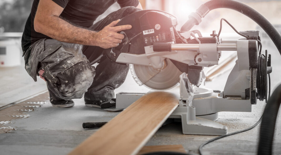 Handwerker schneidet Holzdiele mit der Kappsäge auf der Baustelle und die Späne werden direkt vom Staubsuager abgesaugt